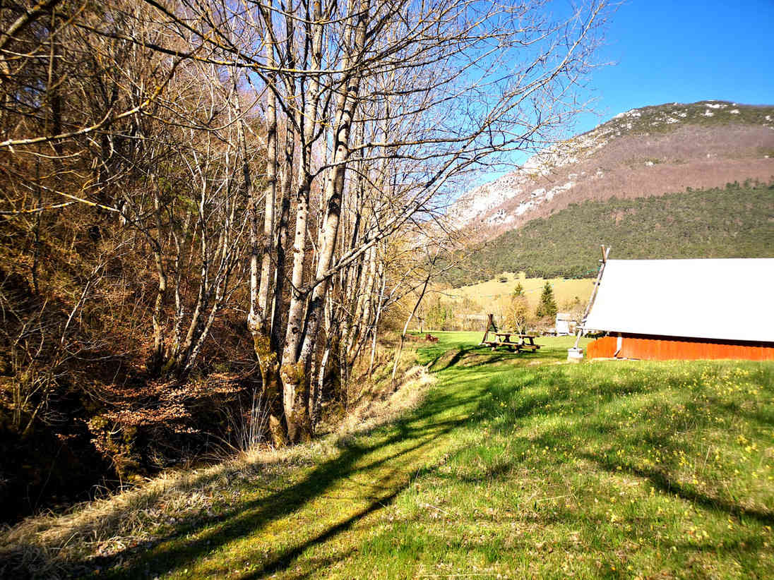 Un paysage pittoresque avec des arbres dénudés, une prairie verdoyante, un banc de parc, et une grange rouge au pied d'une montagne