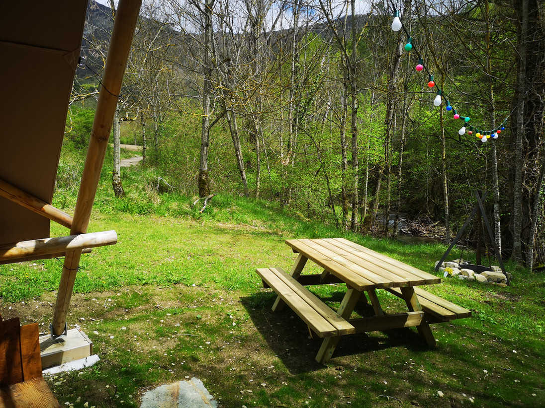 Une table de pique-nique en bois sur une pelouse verte, avec des arbres dénudés et une guirlande de lumières colorées en arrière-plan