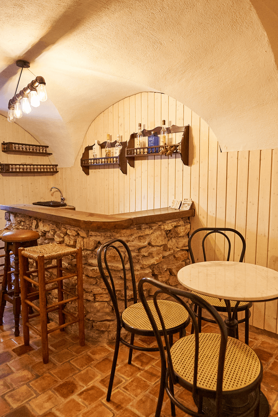 Un coin confortable avec un bar en pierre et bois, deux chaises hautes, une table ronde et 3 chaises, éclairé par des lumières suspendues.