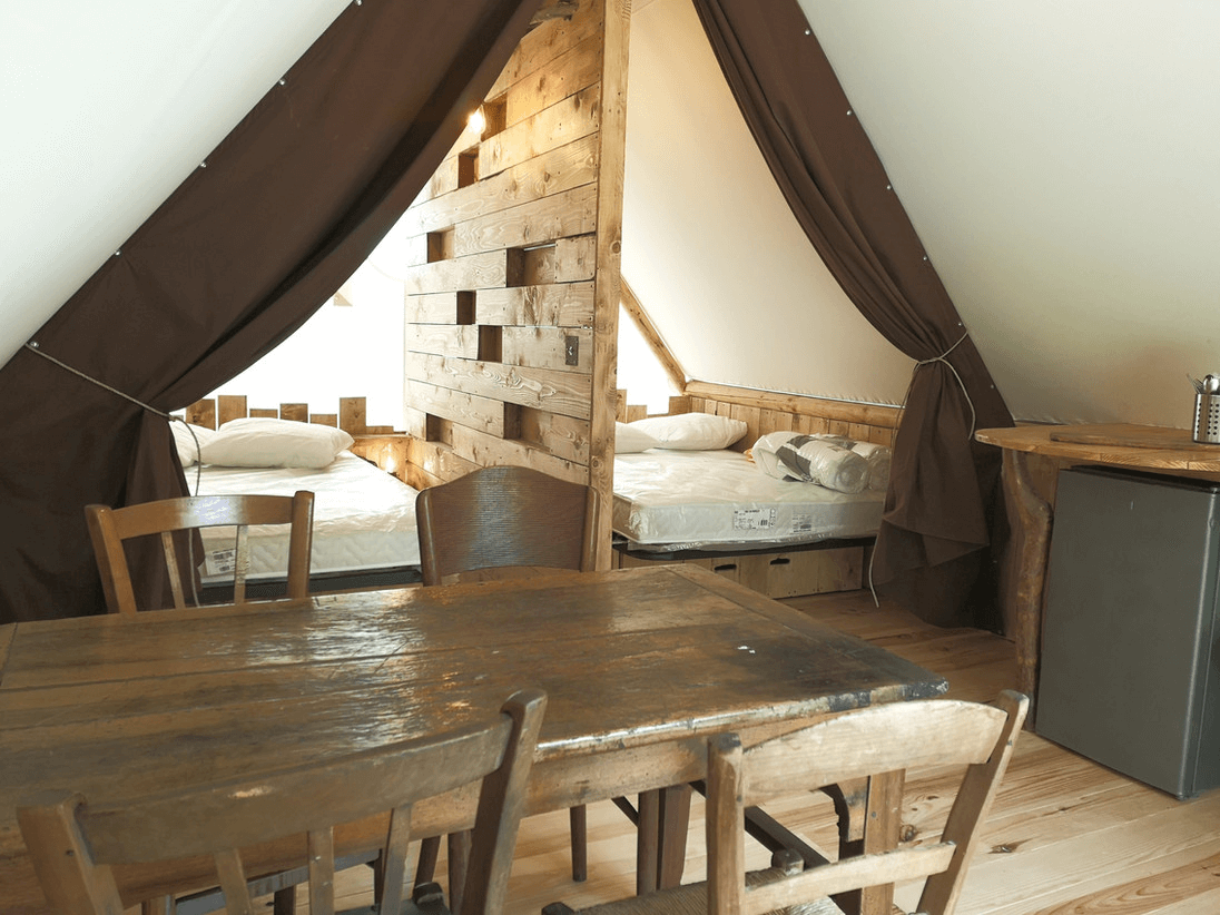Une chambre confortable et rustique avec des lits superposés en bois, un coin repas avec une table et des chaises en bois, le tout sous une tente de toile brune.