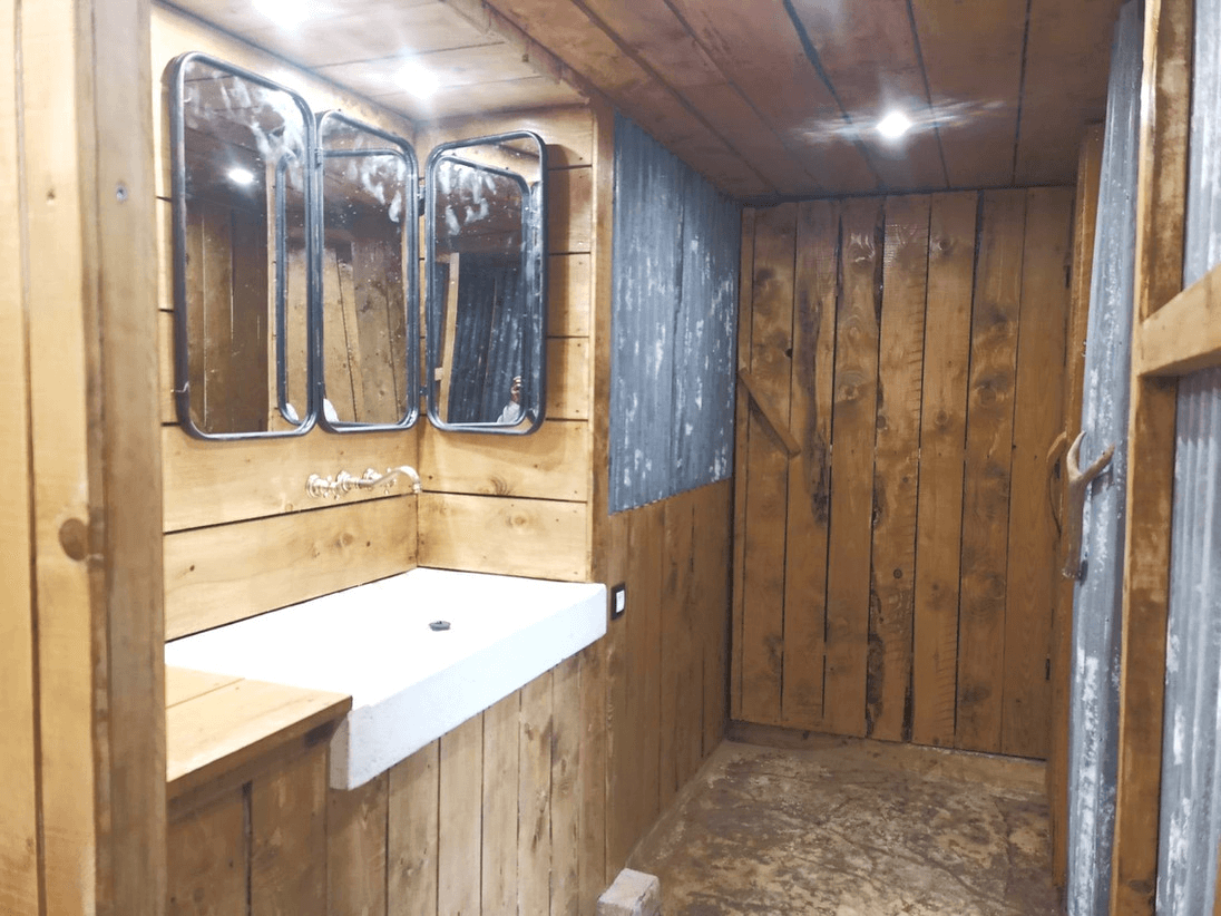 Intérieur en bois d'une petite pièce avec trois miroirs rectangulaires, un comptoir blanc et un sol en béton.